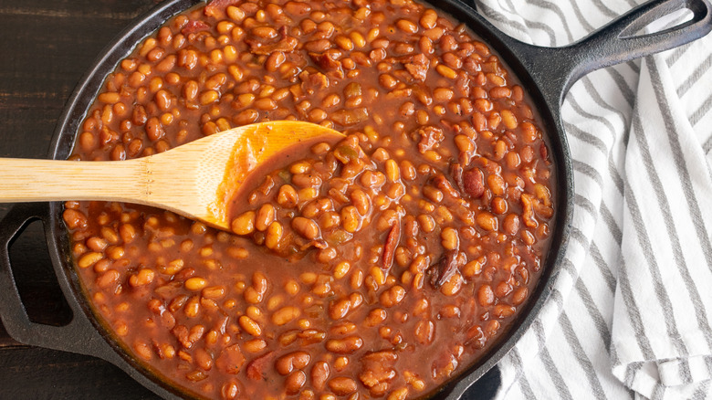 Close up of a skillet of baked beans with a wooden spoon inside