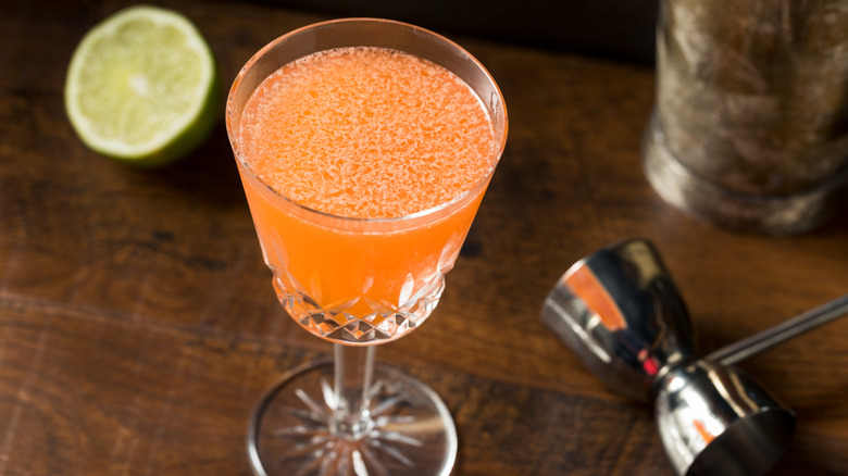 Naked and famous cocktail on table, with a sliced lime and a cocktail jigger