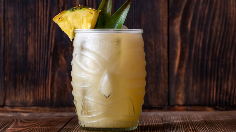 Painkiller cocktail in tiki glass garnished with a pineapple slice and leaves