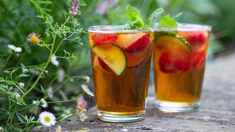 Two Pimms cup cocktails with fruit garnishes surrounded by flowers