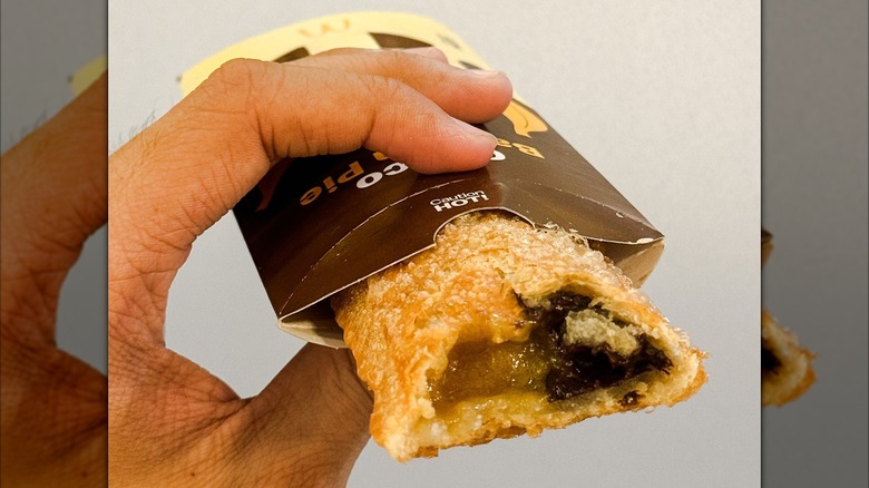A hand holding a chocolate and banana pie in a cardboard wrapper