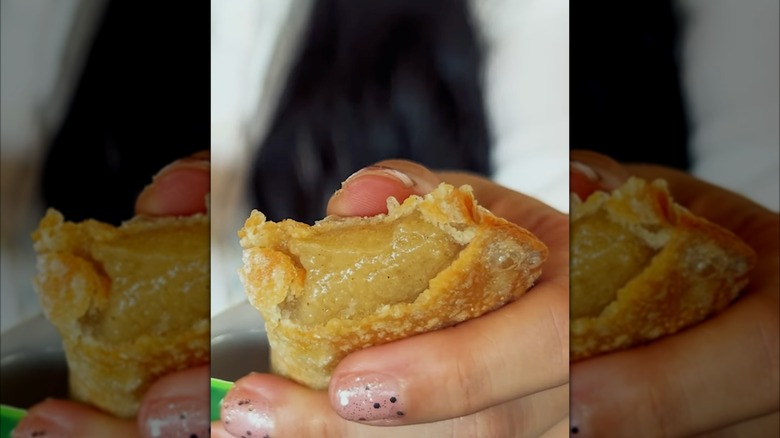 A hand holding a banana pie with a bite in it