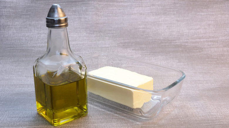 A small glass bottle of olive oil next to a glass container of butter