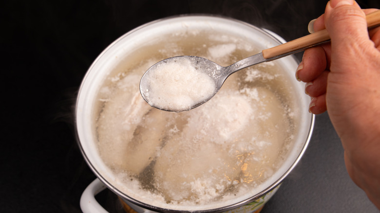 A hand spoons frothy fat off the top of a pot of cooking chicken