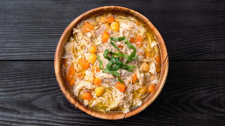 A bowl of chicken noodle soup with carrots and chickpeas topped with a green garnish