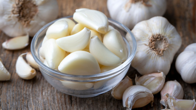 A bowl of peeled garlic cloves next to unpeeled garlic heads