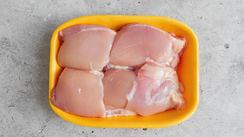 A pack of chicken thighs on a granite counter in a yellow Styrofoam container