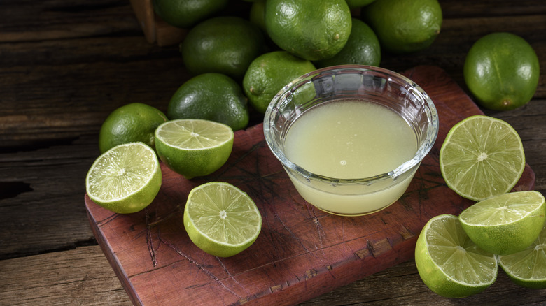 Sliced limes next to a glass container of lime juice on a wooden cutting board