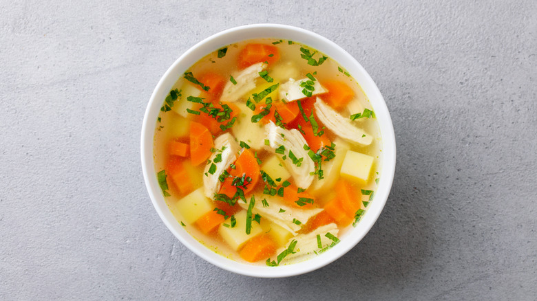 A bowl of chicken soup topped with green herbs as garnish