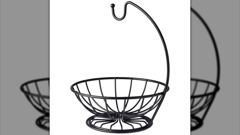 A black metal banana hanger with attached basket underneath against a white background.