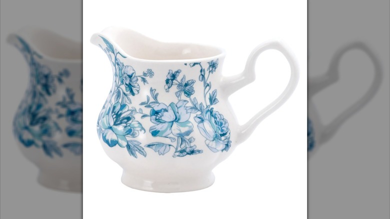 A small white pitcher with blue toile design against a white backdrop.