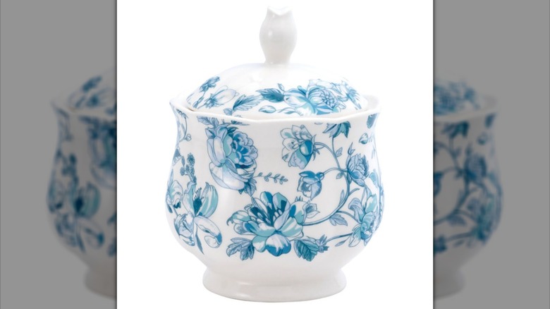 A small white canister with lid and blue toile design throughout against a white background.