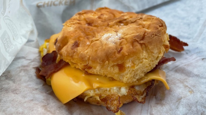 A close up of Jack in the Box biscuit breakfast sandwich with cheese and bacon on branded paper