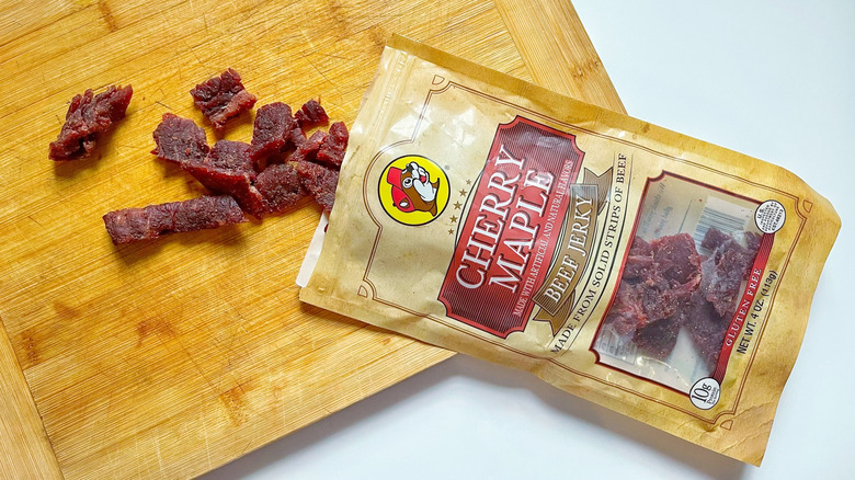 A bag of Cherry Maple jerky with a few pieces on a wooden cutting board