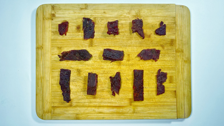 13 pieces of jerky arranged on a wooden cutting board