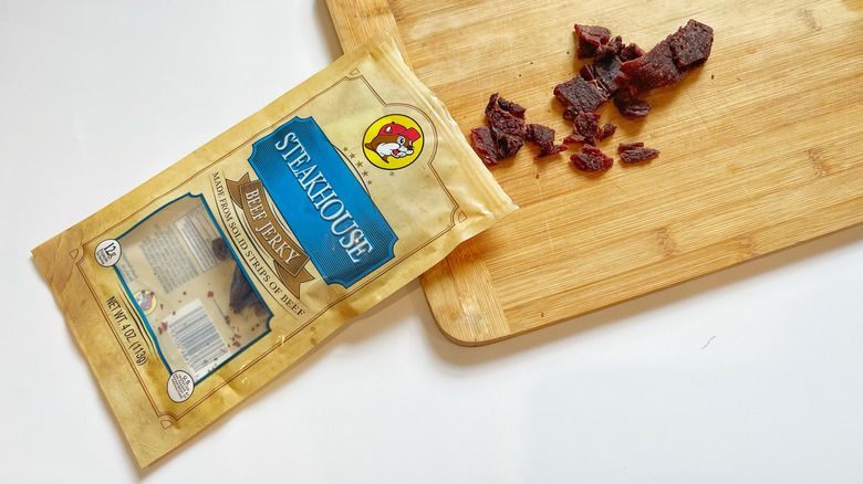 A bag of Steakhouse jerky with its contents spilling on a wooden cutting board