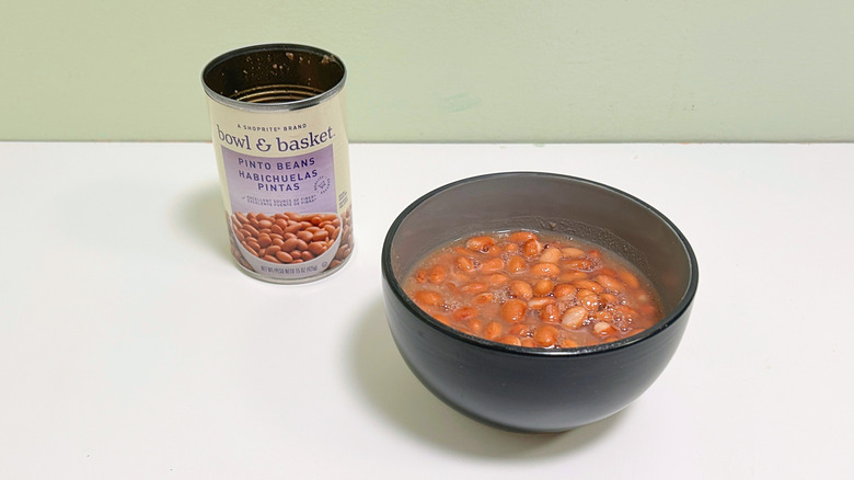 A can of Bowl and Basket Pinto Beans next to a bowl of pinto beans
