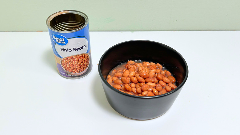 A can of Great Value Pinto Beans next to a bowl of pinto beans