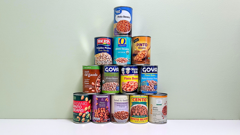 Several cans of pinto beans from different brands stacked together