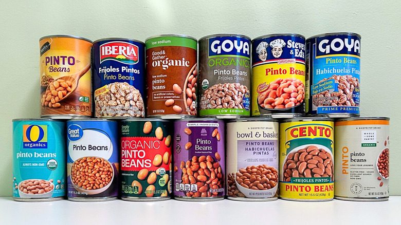 Several cans of pinto beans from different brands stacked together