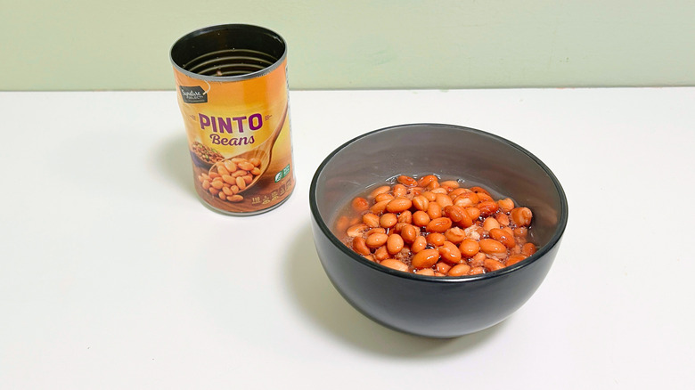 A can of Signature Select Pinto Beans next to a bowl of pinto beans