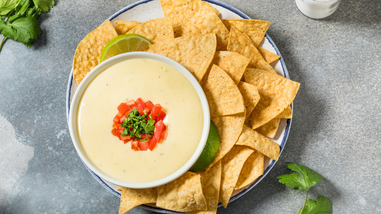 A bowl of queso framed against a plate of tortilla chips