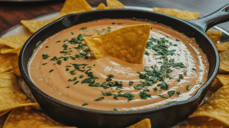 Queso topped with fresh herb garnish with a tortilla chip stuck in the middle