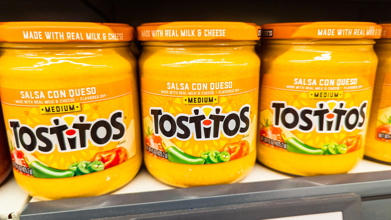 Three jars of Tostitos Medium Salsa Con Queso lined up on a shelf