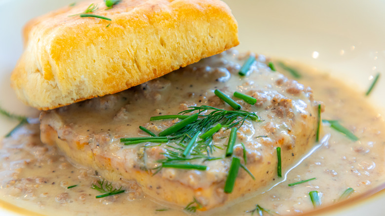 A halved biscuit soaking in gravy with herb garnish is on a plate.