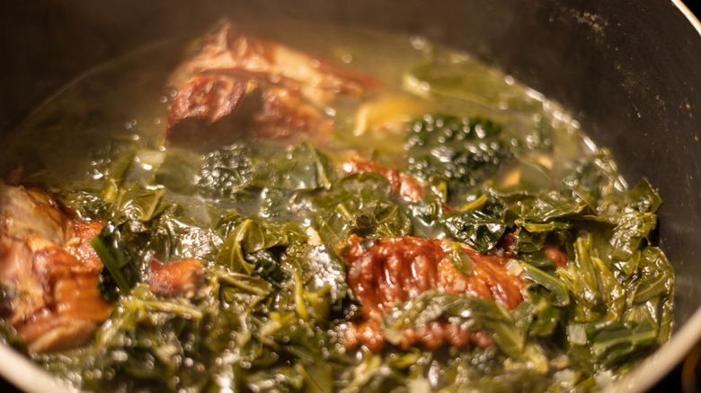 A pot of collard greens with smoked turkey cooks on a stove.