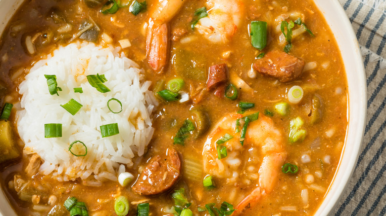 A bowl of shrimp, okra, and sausage gumbo with rice is shown close up.