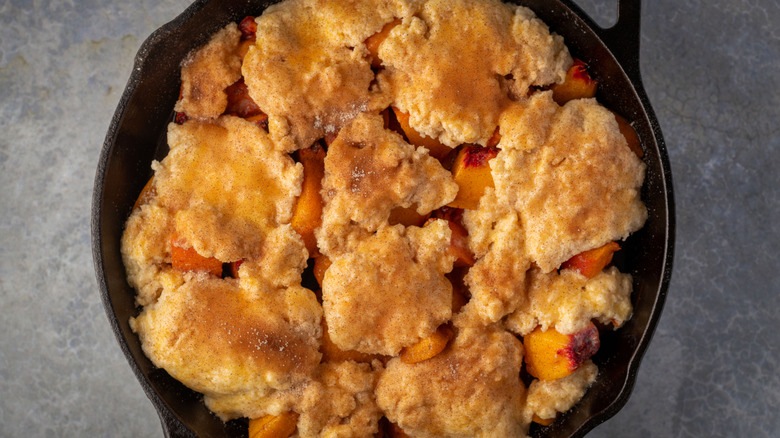 A cast iron skillet of peach cobbler is on a grey background.