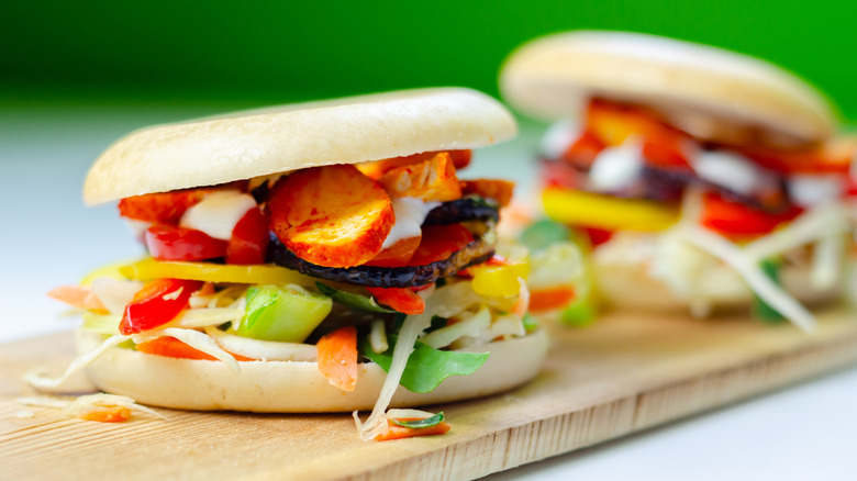 Two roasted veggie bun sandwiches on a wooden board