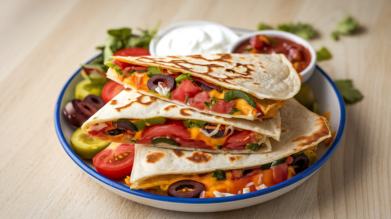 A plate of veggie quesadillas with salsa, sour cream, and salad on a wooden table