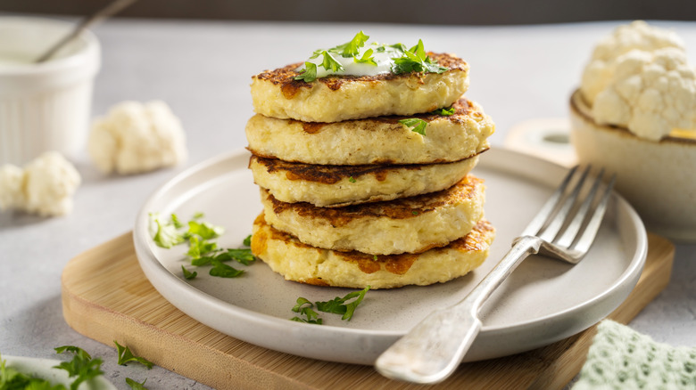 Vegetable fritters stacked up on a white plate with a fork