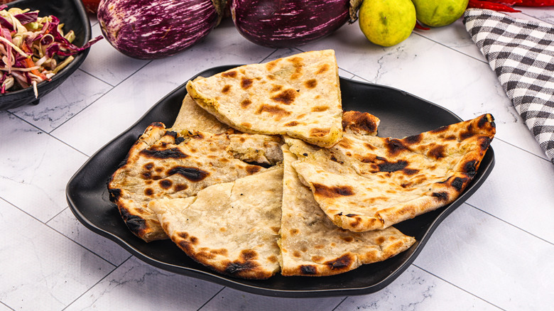 Stuffed paratha on a black plate placed on a white table