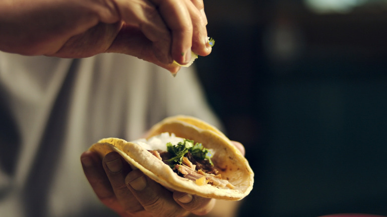 Hand squeezes lime over taco in Taco Chronicles