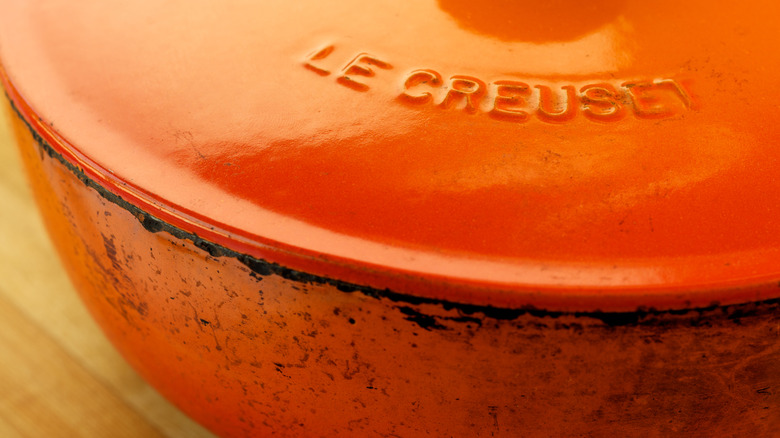 A close-up of an orange Le Creuset dish, displaying its lid and body, with distressed marks along it
