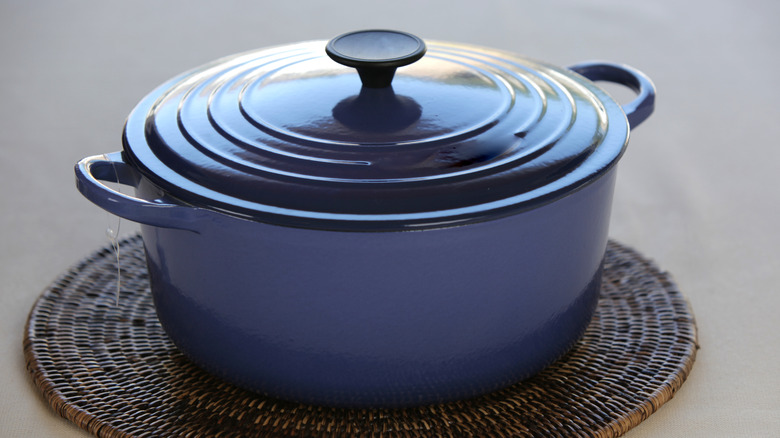 A blue Dutch oven is seen on a heat mat