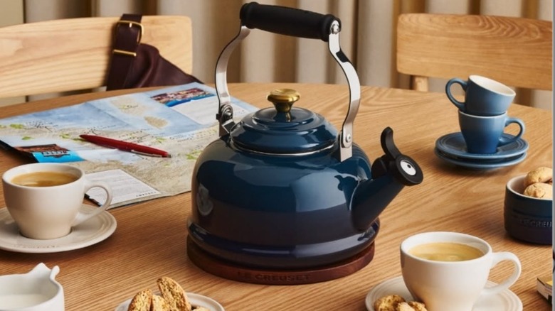 A navy blue Le Creuset Whistling Kettle on a table with cups of tea and pasteries
