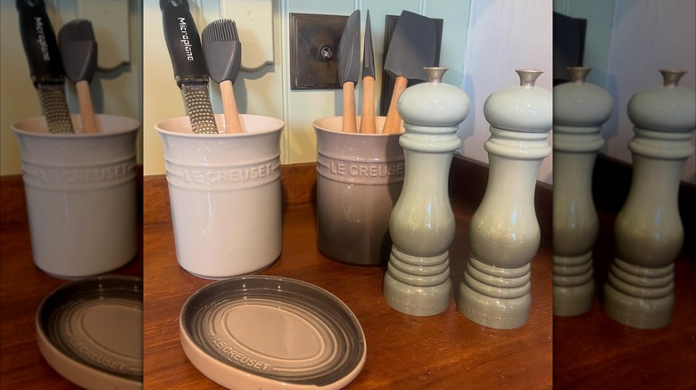 A set of Le Creuset salt and pepper mills, sitting next to utensil containers, spatulas, and various other kitchen tools