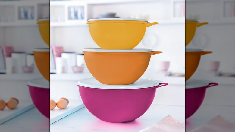 A small yellow, medium orange, and large fuchsia Tupperware bowls with white lids stacked