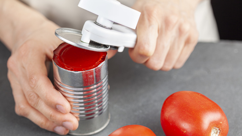Hands use a can opener to open a can of tomato paste