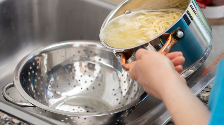 Hands pour boiled pasta and water into metal colander