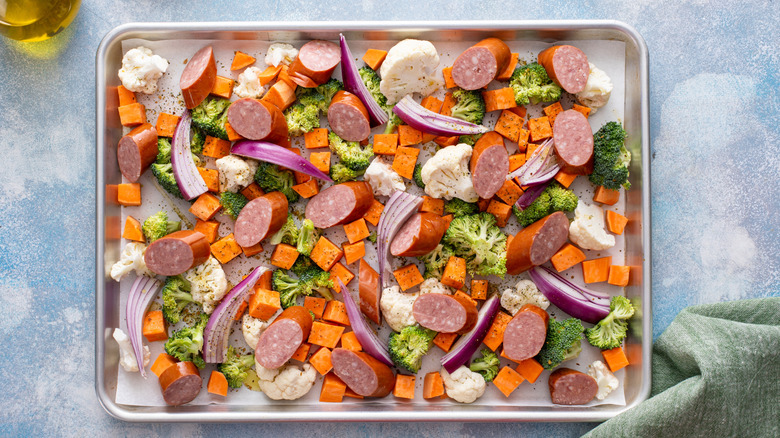 Sliced sausage and vegetables on sheet pan with parchment paper
