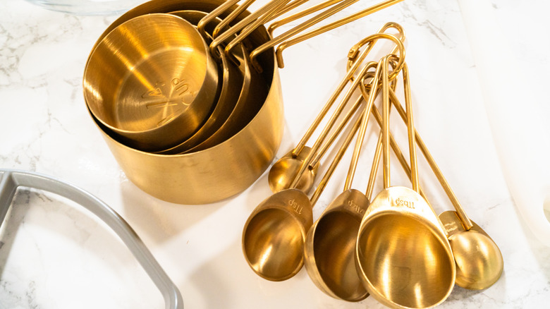 Golden sets of measuring cups and spoons on marble surface