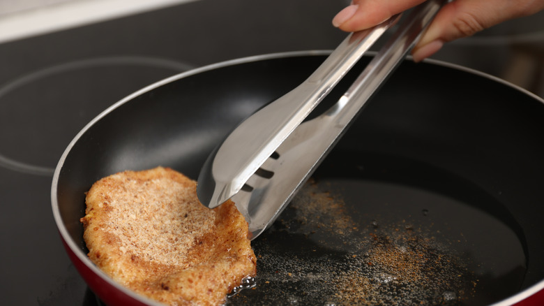 Hand uses tongs to grip fried meat in pan