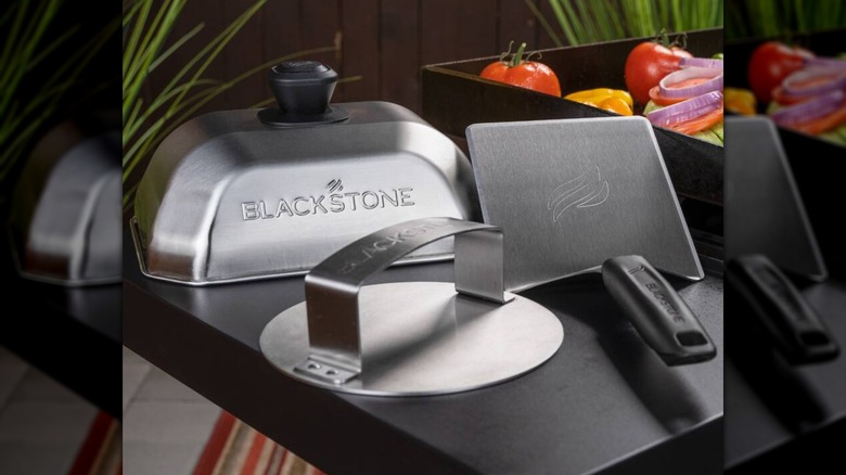 Blackstone 3-Piece Smash Burger Kit on a grill, next to various vegetables