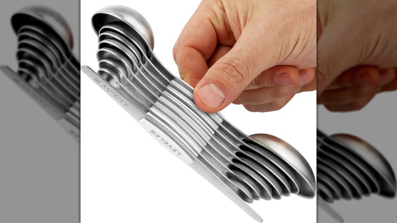 A hand holding the Zulay Kitchen Magnetic Measuring Spoon Set on a white background