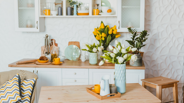 Kitchen with decorative plates, cups, vases, and flowers in spring colors like white, orange, and blue
